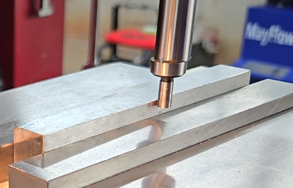 Mechanical edge finder rotating in a milling machine spindle, about to make contact with the workpiece surface for edge detection.