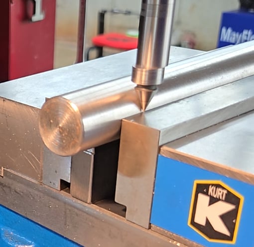 Close-up of an edge finder tip deflecting after touching the edge of a clamped workpiece, indicating the moment to zero the DRO.